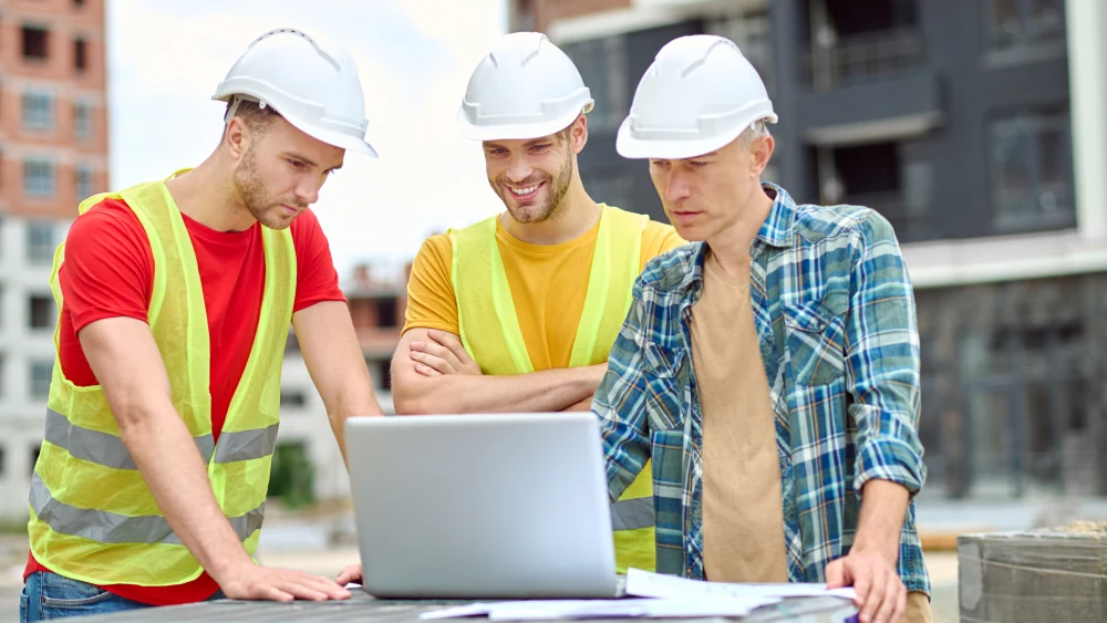 important information three men protective helmet looking laptop with interest while standing construction site day